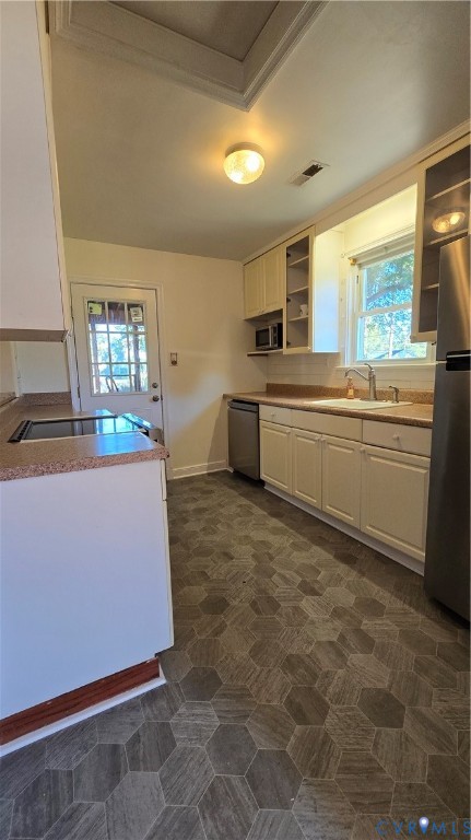 Kitchen featuring white shaker-style cabinetry, stainless steel appliances, hexagonal patterned flooring, integrated countertop, and a window above the basin