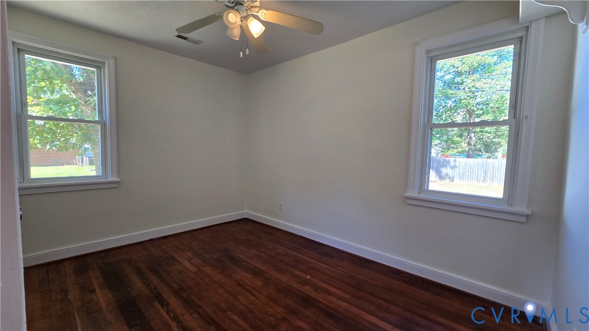 Interior space featuring wood-finish flooring, two double-hung windows, and a ceiling-mounted light fixture with a central fan