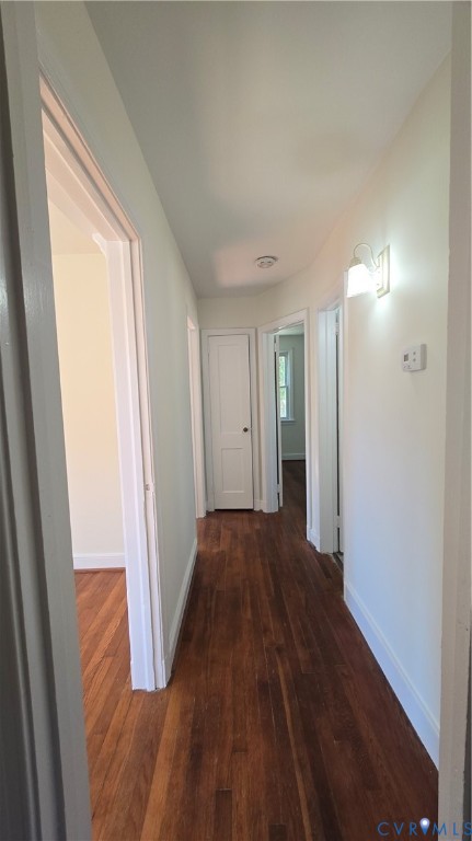 Interior hallway featuring wood-finish flooring, white paneled interior doors, and wall-mounted light fixtures Interior hallway featuring wood-finish flooring, white paneled interior doors, and wall-mounted light fixtures