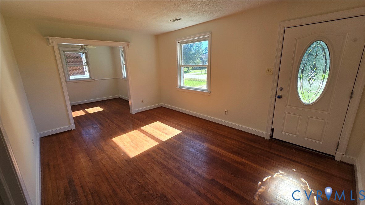 Interior space featuring wood-finish flooring, white wall trim, and an exterior door with an oval glass inset Interior space featuring wood-finish flooring, white wall trim, and an exterior door with an oval glass inset