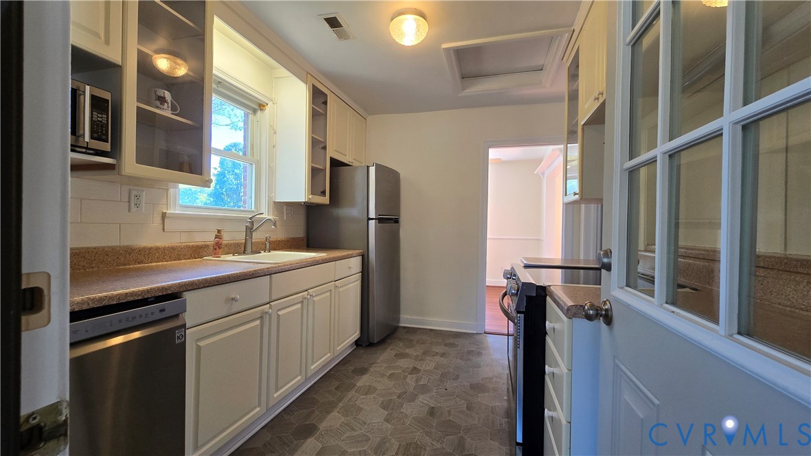 Kitchen featuring white cabinetry, stainless steel appliances, tile backsplash, and patterned flooring