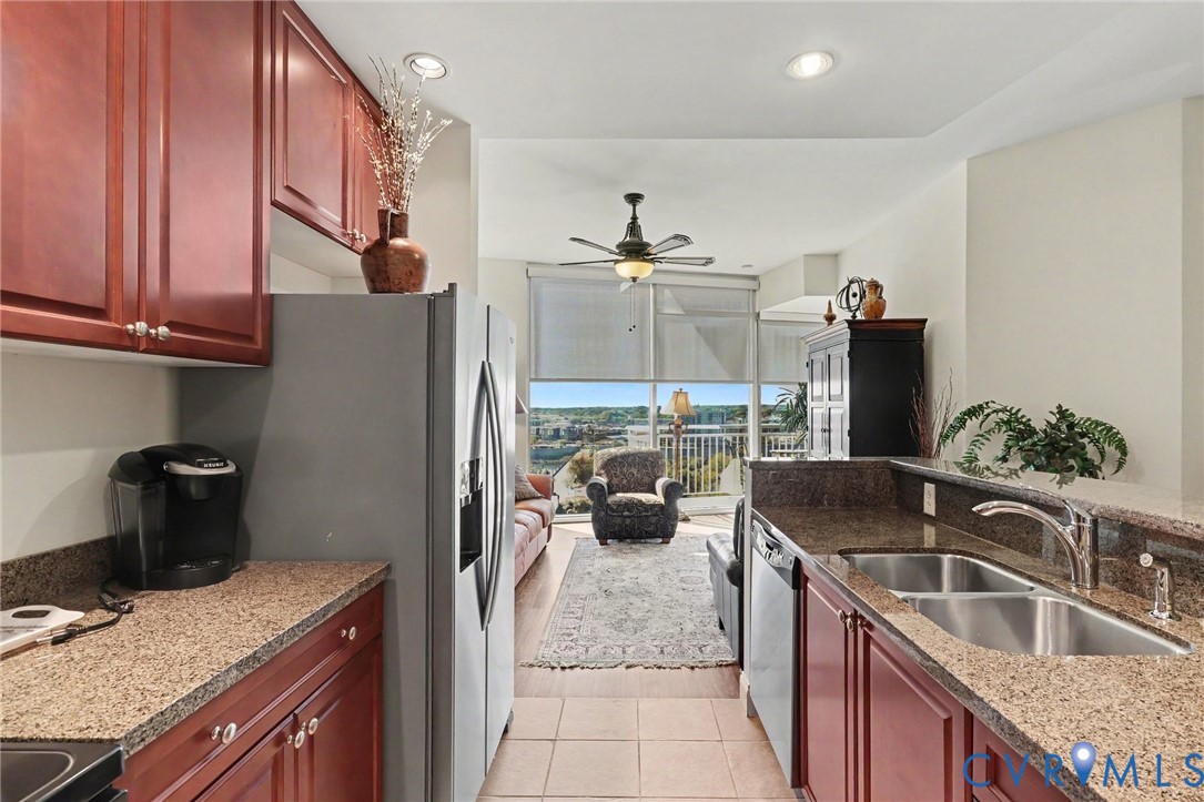 Kitchen featuring dark wood-finish cabinetry, stone-finish countertops, stainless steel appliances, a dual-basin undermount sink, and recessed lighting