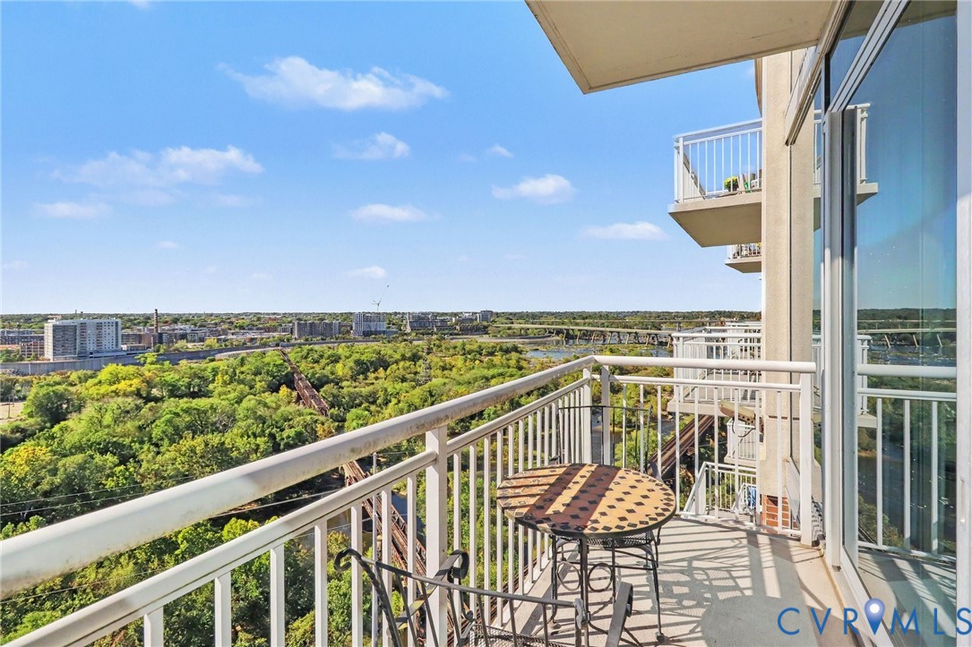 Private balcony featuring a metal railing and floor-to-ceiling glass sliding doors, overlooking an expansive natural landscape and urban skyline