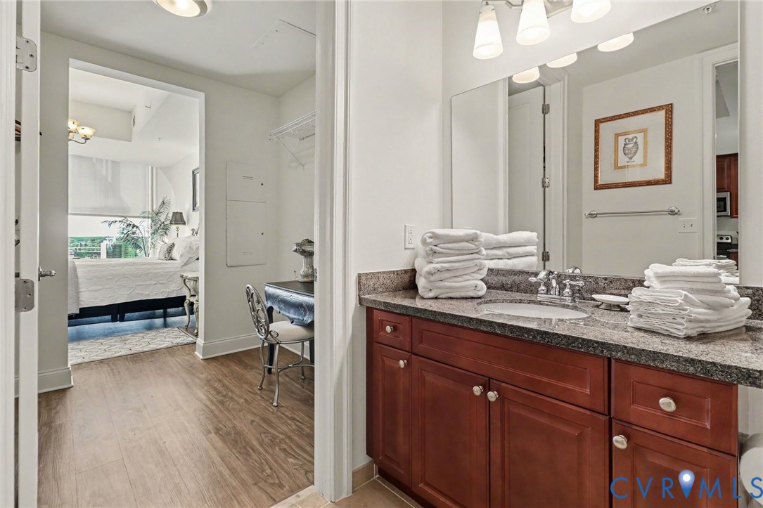 Bathroom vanity featuring stained wood cabinetry, stone countertop, integrated sink, and full-width wall-mounted mirror