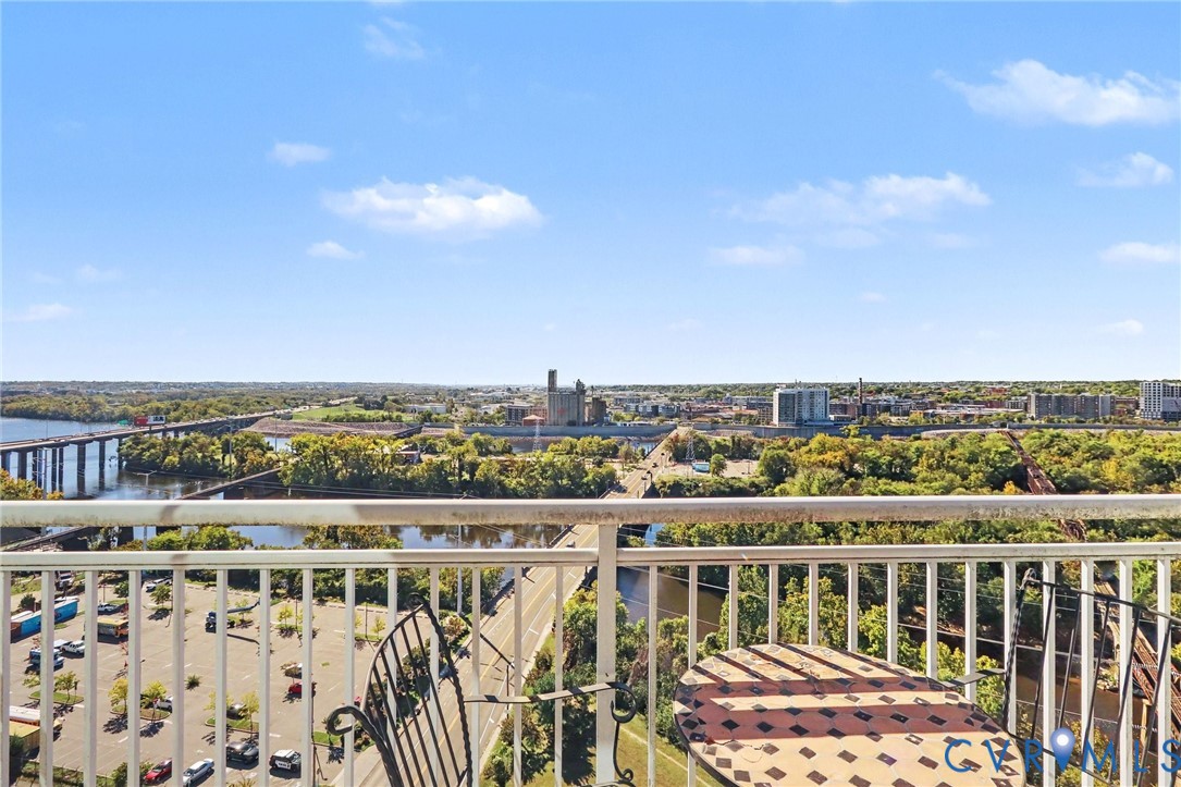 Elevated balcony with a metal railing overlooking expansive terrain including a river, bridge, and urban landscape