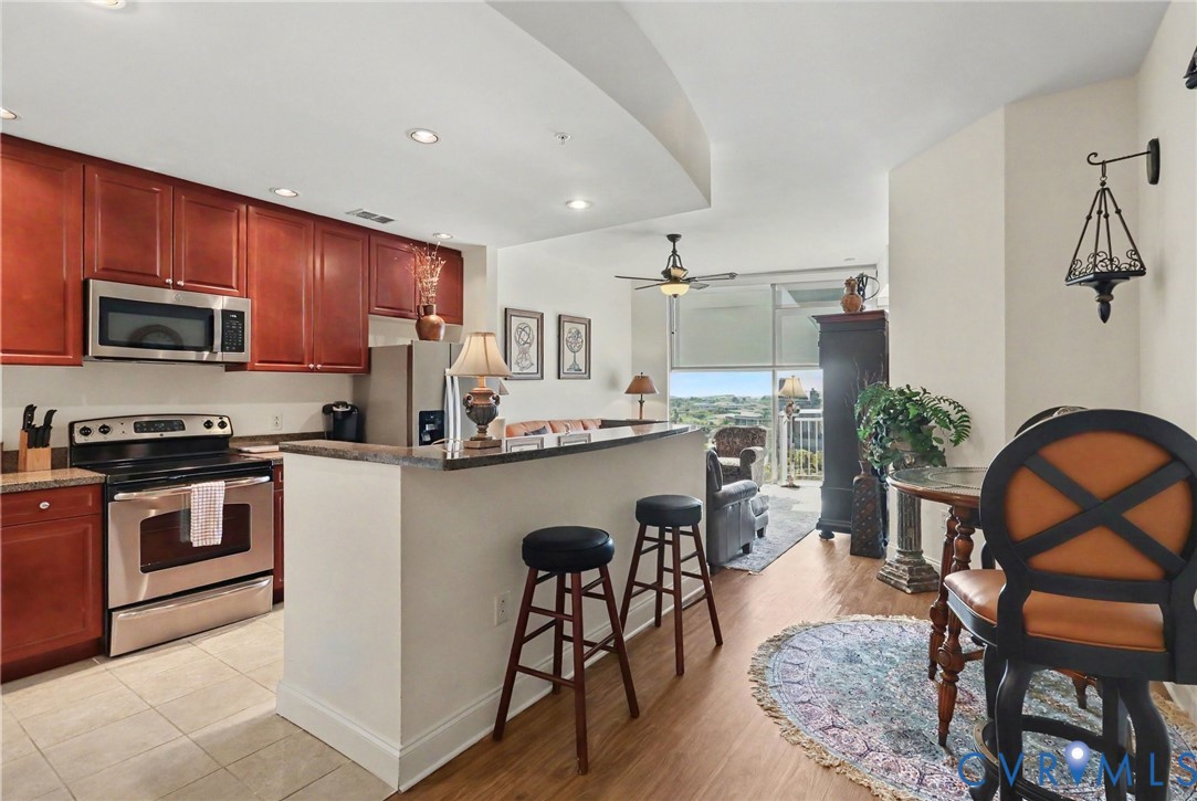 Kitchen featuring stained wood cabinetry, a breakfast bar with stone-surface countertop, stainless steel appliances, tile flooring, and floor-to-ceiling windows