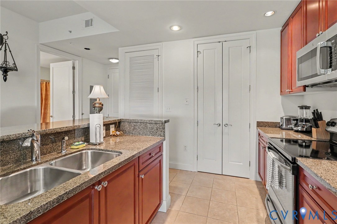 Kitchen featuring cherry-finish cabinetry, stone-surfaced countertops, a dual-basin stainless steel sink with a high-arch faucet, tile flooring, and recessed lighting