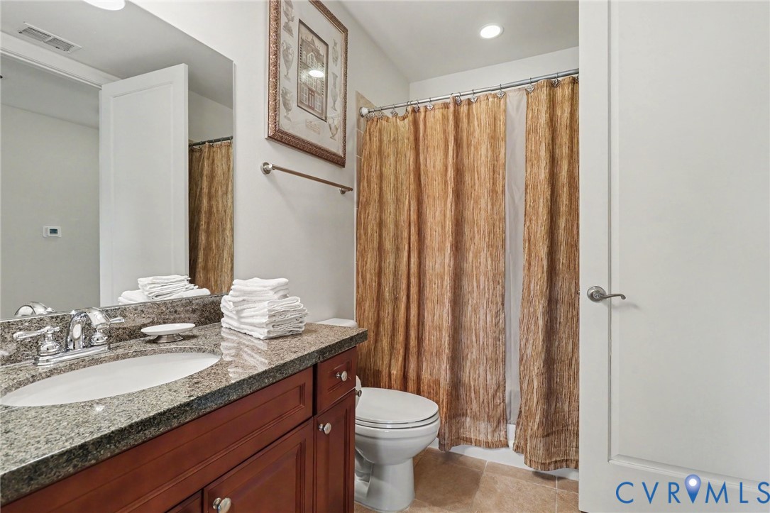 Bathroom featuring a vanity with stone-finish countertop, undermount sink, chrome faucet, wood-finish cabinetry, and recessed lighting