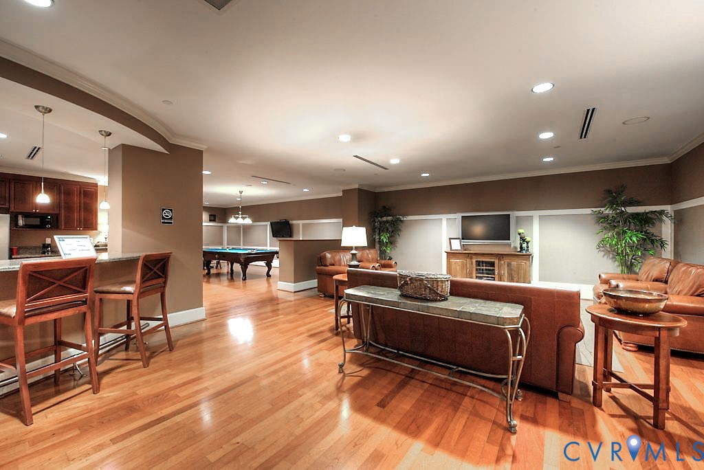 Open-concept recreation area featuring wood-finish flooring, recessed lighting, crown molding, chair rail wainscoting, and an integrated bar with pendant lighting
