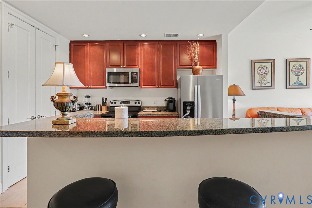 Kitchen featuring wood cabinetry, stone countertops, stainless steel appliances, and a breakfast bar