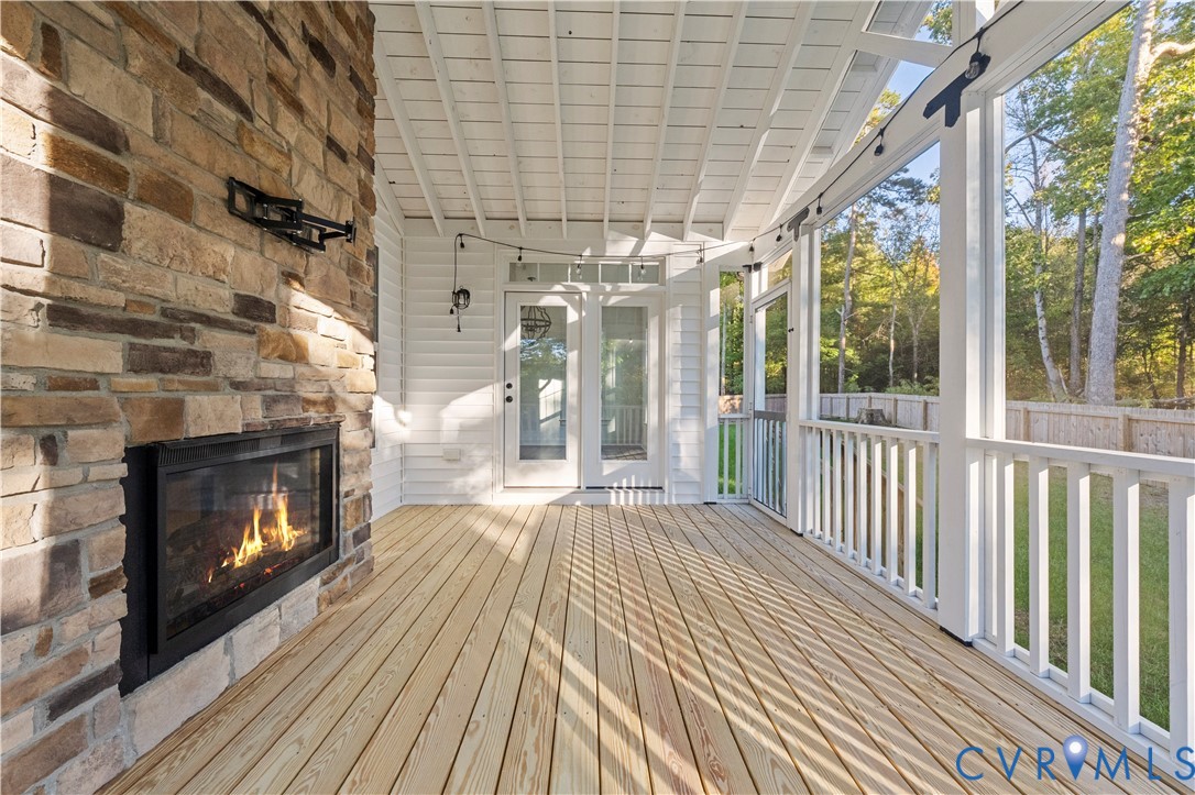 Covered porch featuring a wood-plank deck, stone-veneer fireplace with a built-in insert, white horizontal siding, and white wooden railing