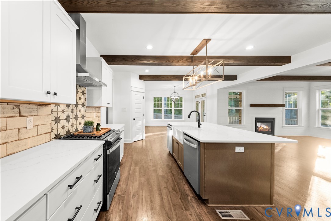 Kitchen featuring white shaker-style cabinetry, quartz countertops, a patterned tile backsplash, wood-finish flooring, and exposed timber ceiling beams