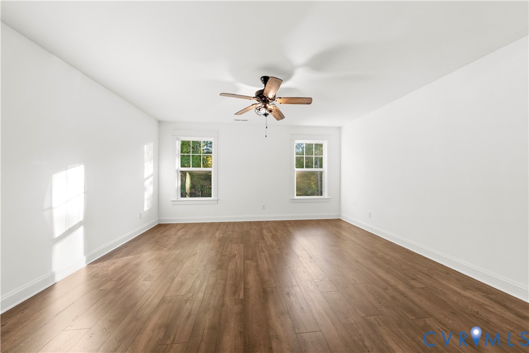 Interior space featuring wood-finish flooring, white walls, dual windows, and a ceiling fan with light fixture