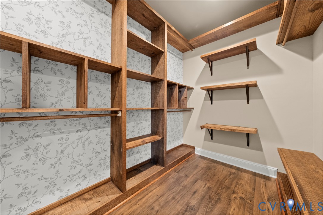 Custom storage space featuring built-in wood shelving, patterned wallpaper accents, wood-finish flooring, and wall-mounted wooden shelves with metal brackets