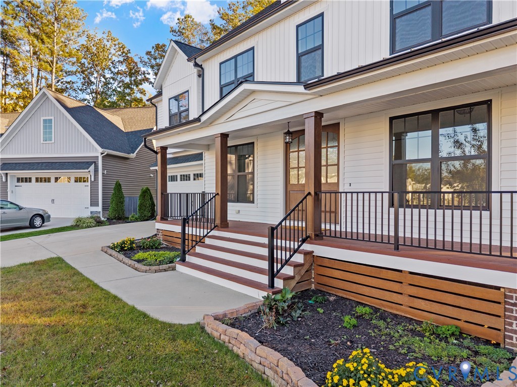 Modern farmhouse exterior featuring horizontal siding, a covered porch with wood-finish decking, dark metal railings, and decorative wood-slat skirting