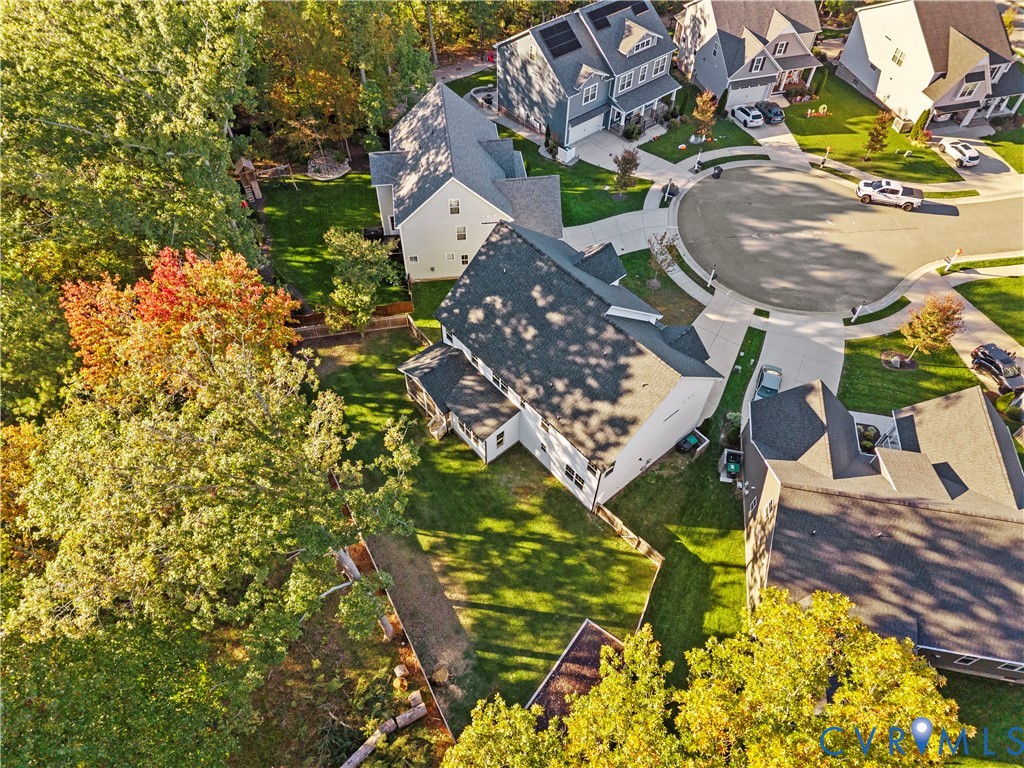 Aerial perspective of a multi-level suburban residence featuring an asphalt shingle roof, concrete driveway, and expansive grass-covered backyard enclosed by privacy fencing