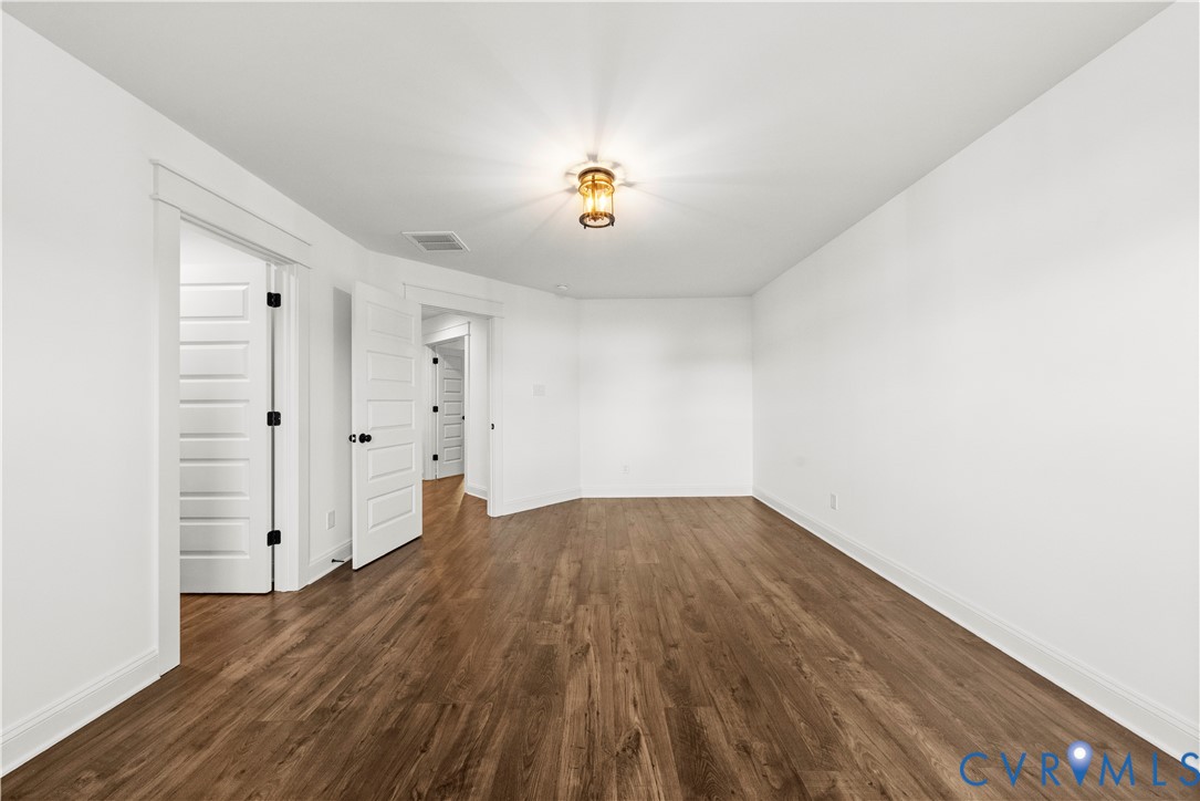 Room featuring wood-finish flooring, white walls, four-panel interior doors with matte black hardware, and a center-mounted ceiling light fixture