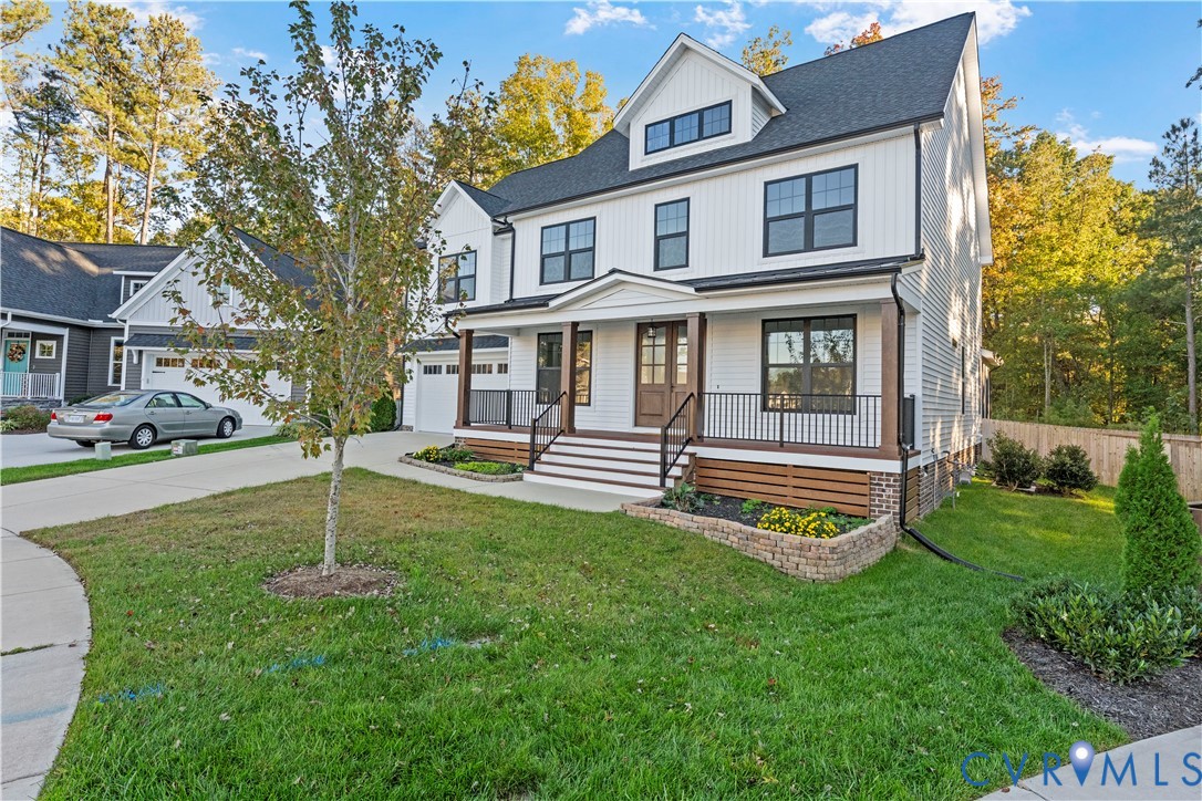 Two-story board-and-batten exterior featuring a covered front porch with metal railing, stacked stone garden beds, and multi-pane windows
