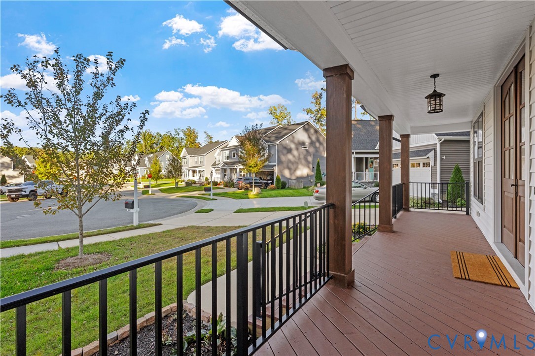 Covered front porch featuring wood-finish decking, black metal railings, square architectural columns, and a hanging outdoor light fixture