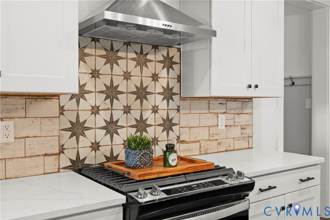 Kitchen featuring white cabinetry, quartz countertops, a patterned tile backsplash, and a stainless steel range hood