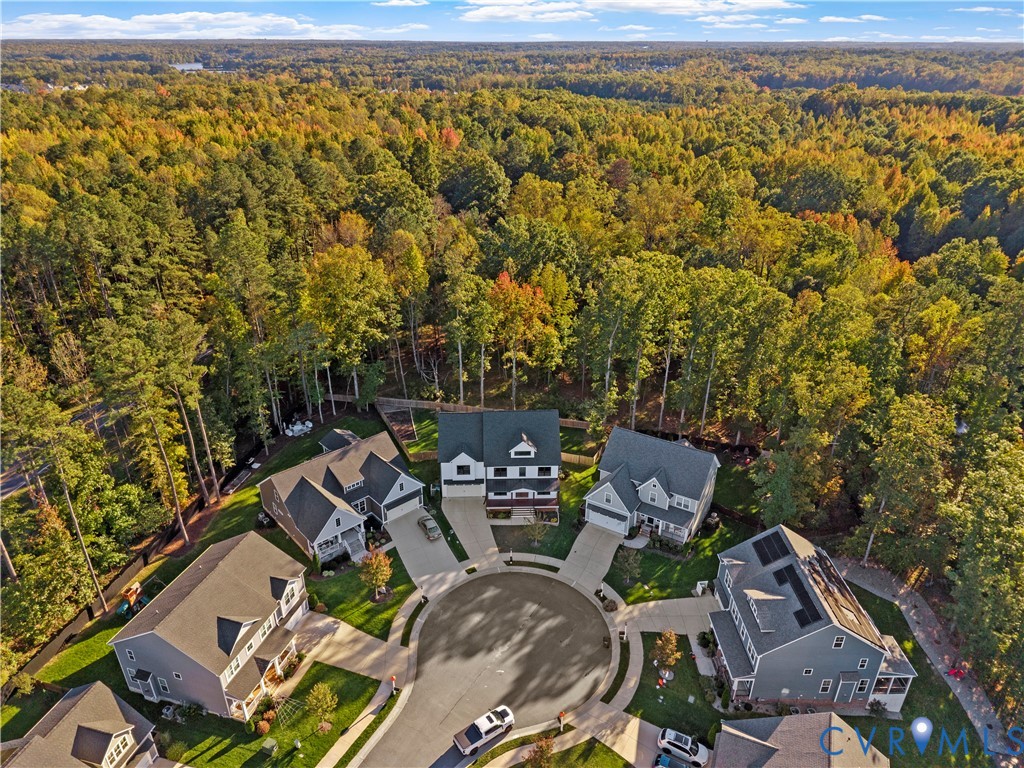 Aerial perspective of a suburban cul-de-sac featuring multi-story residential dwellings, concrete driveways, and surrounding dense woodland