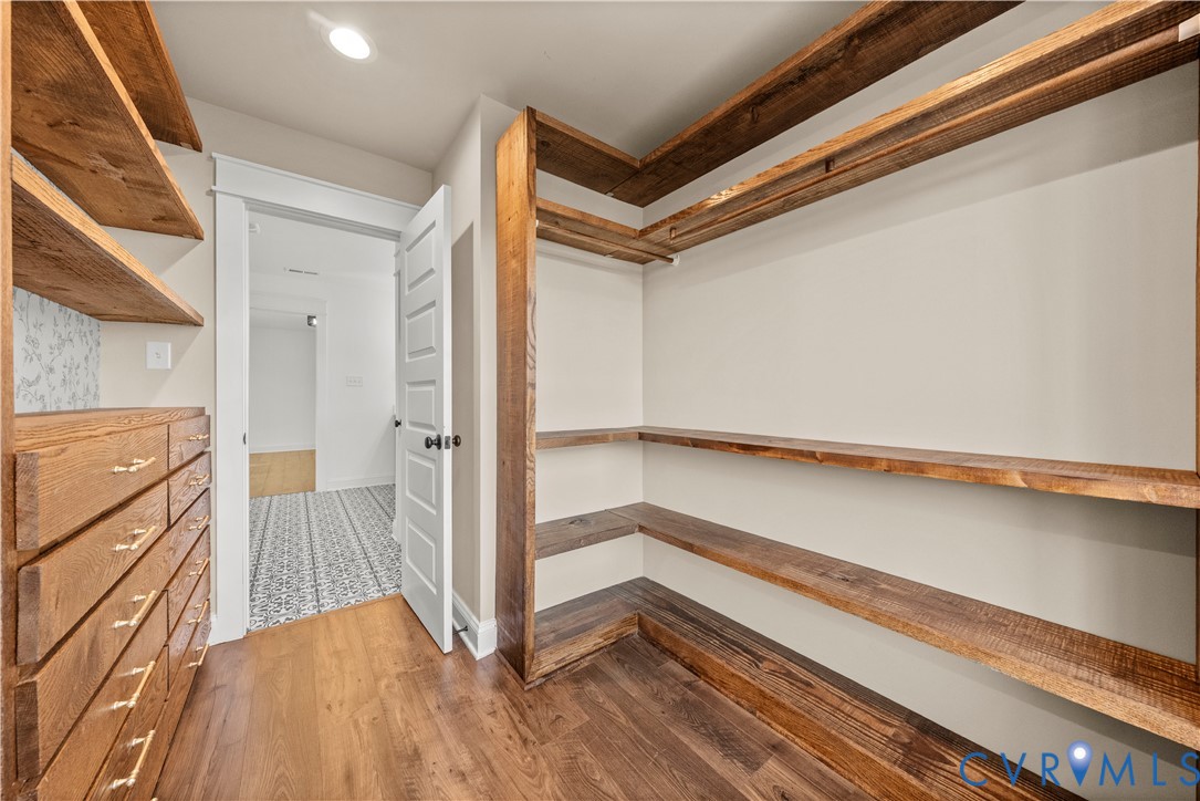 Custom reach-in closet featuring natural wood-finish shelving, built-in drawer units with metallic hardware, and wood-finish flooring
