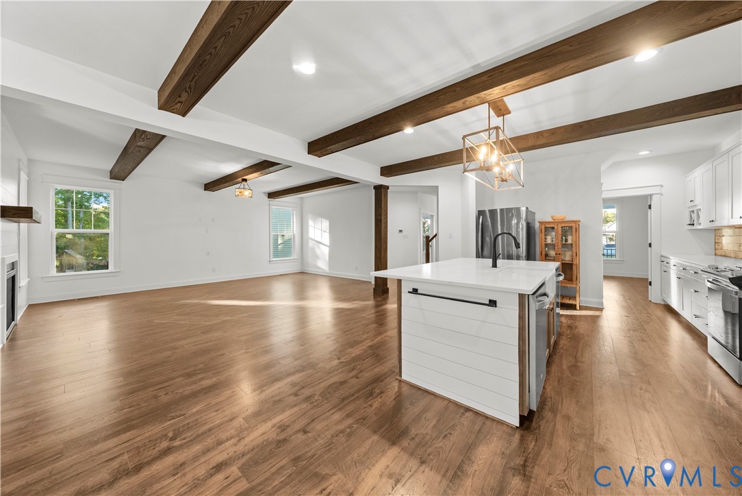 Open-concept interior featuring exposed wood ceiling beams, white cabinetry, a center island with a shiplap facade and solid surface countertop, and wood-finish flooring