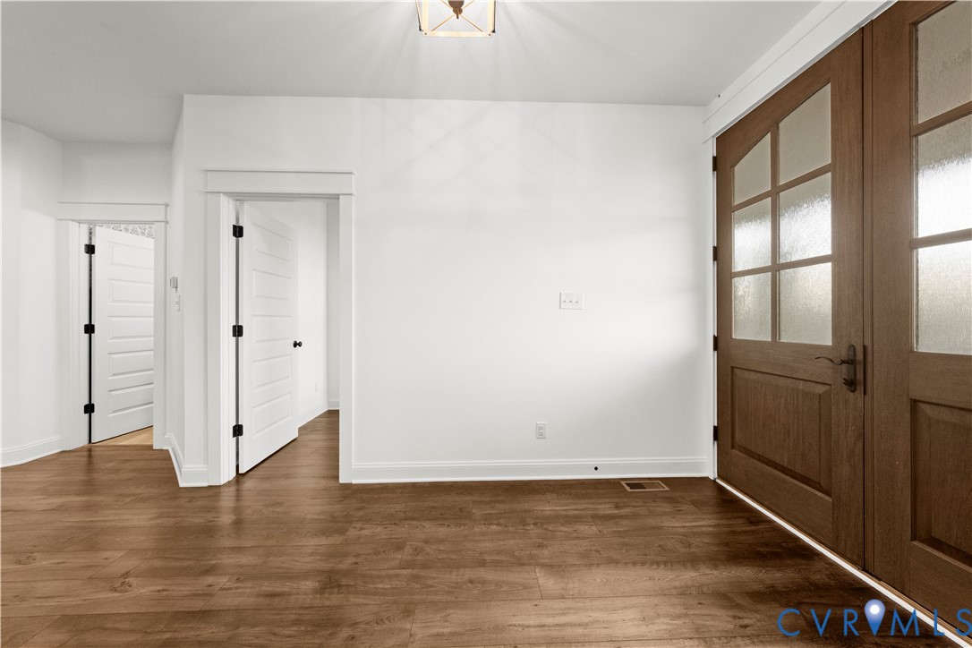 Double entry doors with multi-lite frosted glass panels, wood-finish flooring, two-panel interior doors with dark hardware, and a ceiling-mounted geometric light fixture