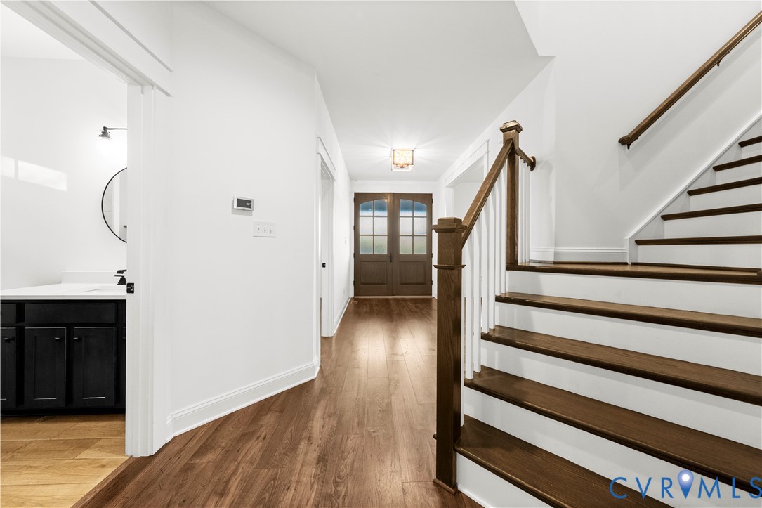 Entry foyer featuring double glass-paneled front doors, wood-finish flooring, and a staircase with stained wood treads and white balusters