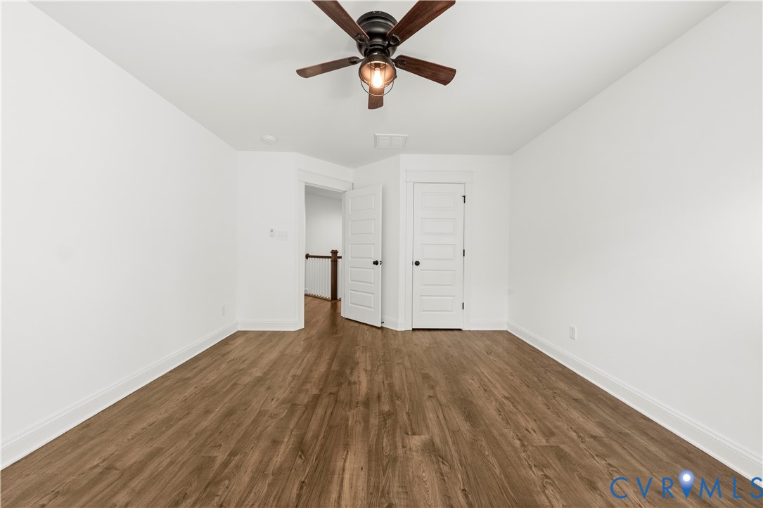 Interior room featuring wood-finish flooring, a multi-blade ceiling fan with integrated lighting, and white five-panel interior doors