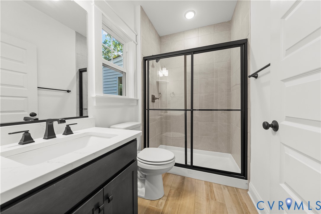 Bathroom featuring a vanity with a white countertop, matte black fixtures, wood-finish flooring, and a glass-enclosed shower with tiled surround