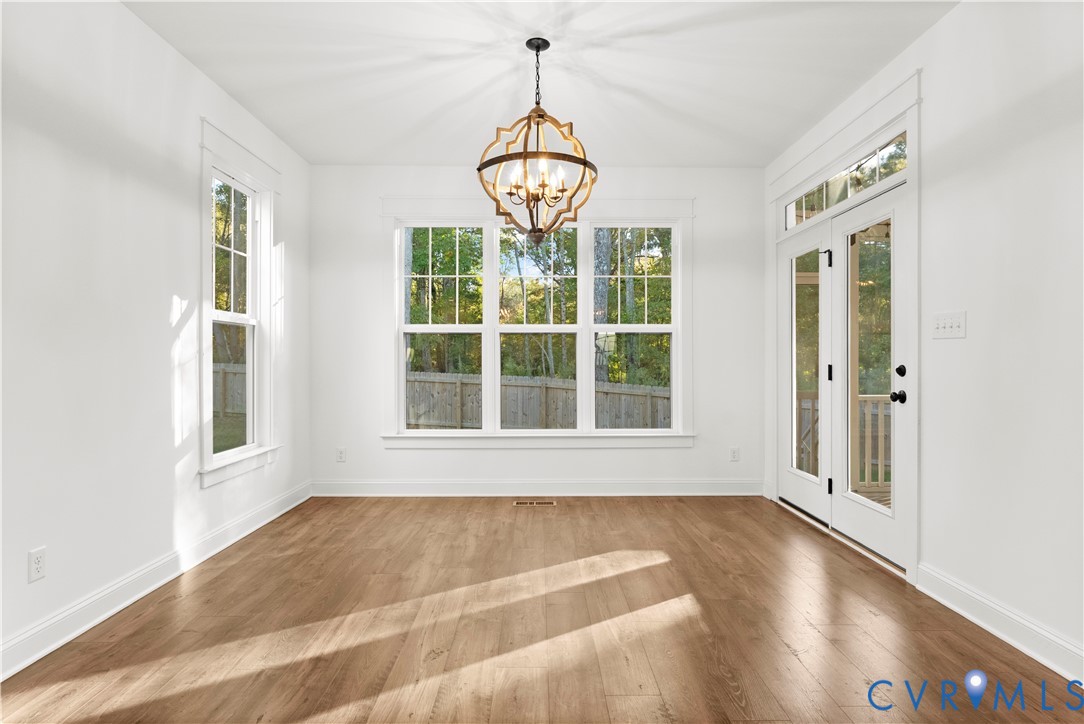 Sun-filled interior featuring wood-finish flooring, a decorative metal-frame chandelier, large multi-pane windows, and double glass-panel doors with transom window