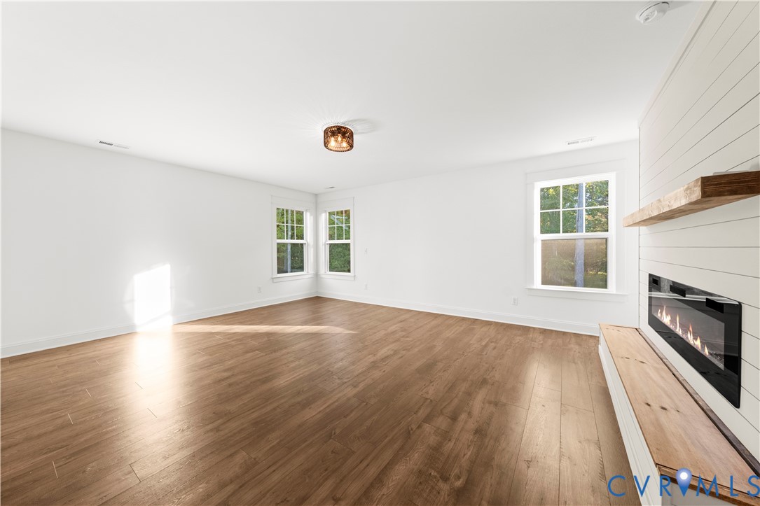 Wood-finish flooring, white shiplap accent wall, built-in fireplace, natural wood mantel, and multi-pane windows