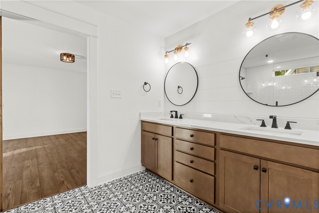 Double vanity with wood-finish cabinetry, solid-surface countertops, circular wall-mounted mirrors, matte black fixtures, and patterned tile flooring