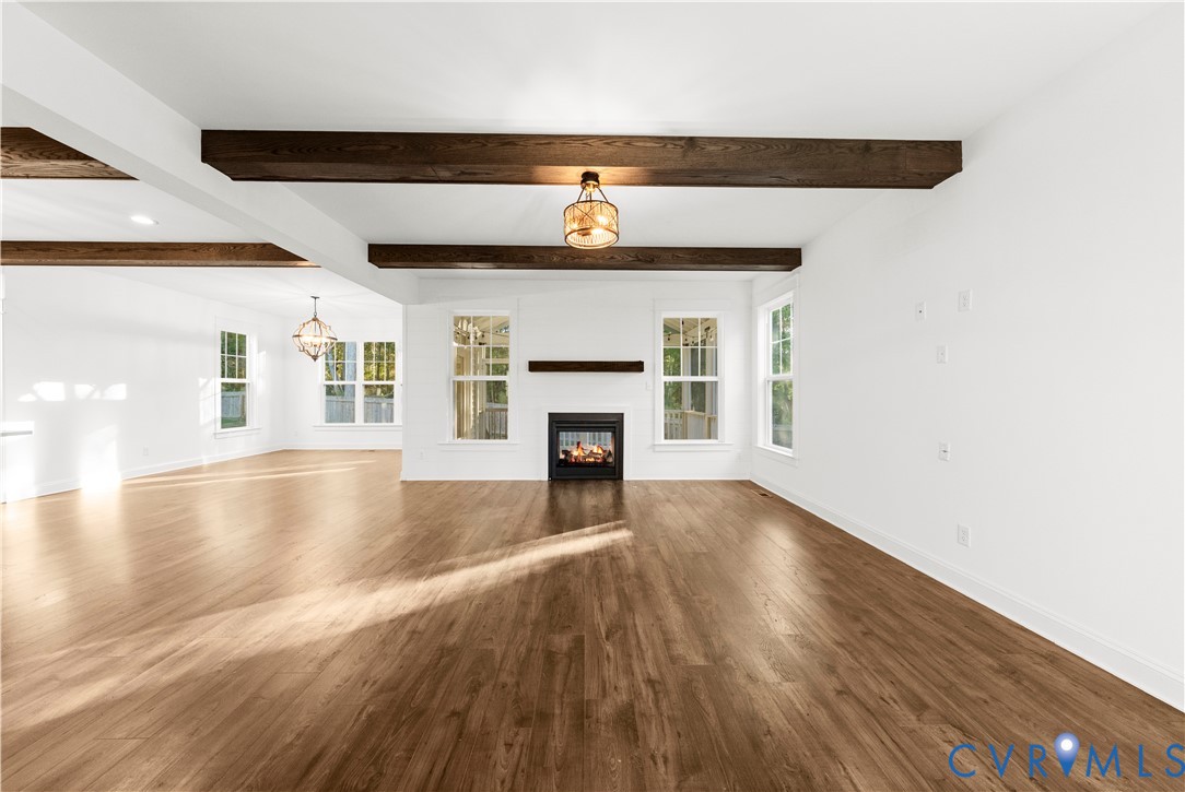Open-concept space featuring wood-finish flooring, exposed stained-wood ceiling beams, a central fireplace with a wood mantel, and multiple multi-pane windows