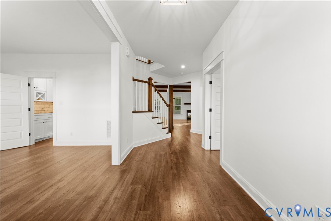 Interior entry featuring wood-finish flooring, a staircase with a wooden handrail and white balusters, and multi-panel doors with matte black hardware