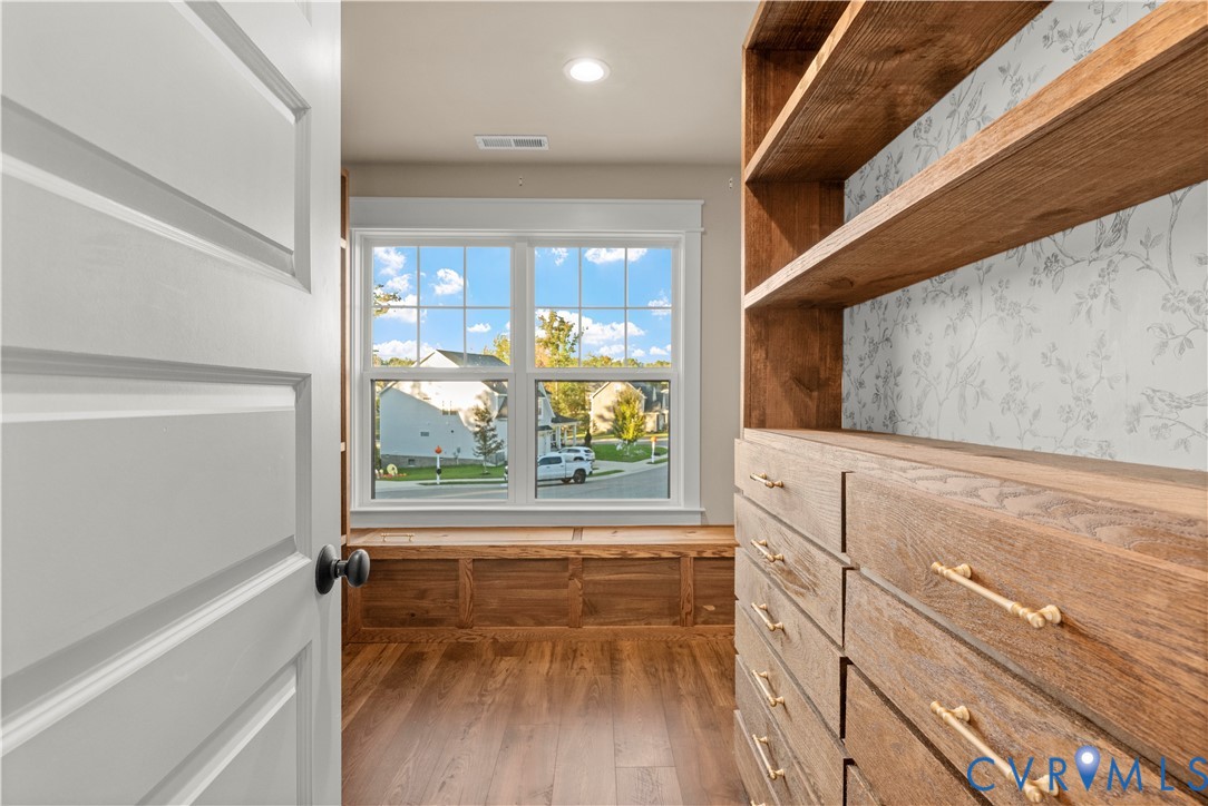 Built-in wooden cabinetry featuring open shelving and soft-close drawers with brass-finish hardware, wood-finish flooring, and a custom window seat