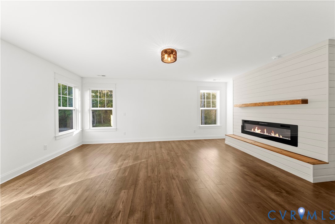 Wood-finish flooring, white shiplap accent wall, built-in linear fireplace, natural wood mantel and hearth, and multi-pane windows