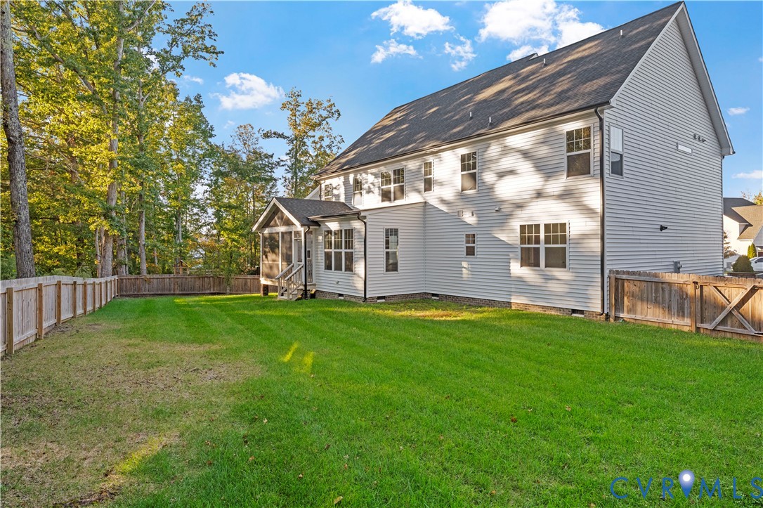 Spacious backyard featuring a manicured lawn, full wood fencing, and a covered screened-in porch with staircase access