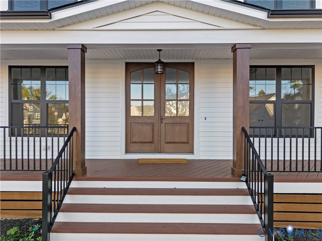 Covered front porch featuring wood-finish decking, structural support columns, metal railing, and double-entry doors with glass pane detailing