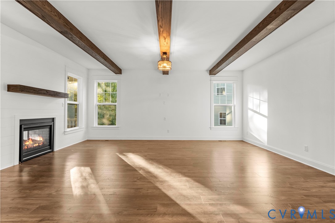 Living area featuring wood-finish flooring, exposed stained-wood ceiling beams, wood-trimmed fireplace mantel, and multipane windows