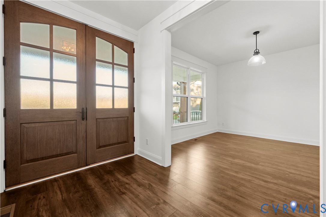 Double wooden entry doors with glass panels, wood-finish flooring, and a pendant light fixture