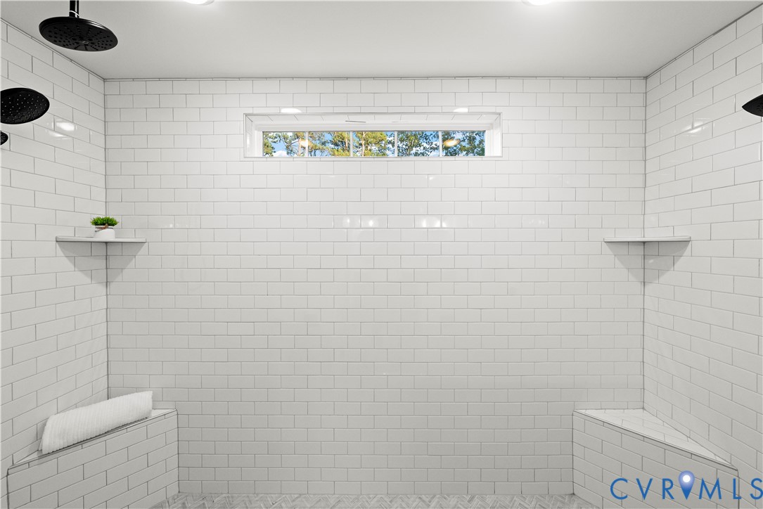Walk-in shower featuring white subway tile surround, dual wall-mounted rainfall shower heads, integrated stone-topped bench seating, and a transom window
