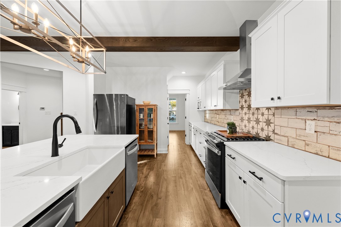 Kitchen featuring white cabinetry, quartz countertops, a farmhouse-style apron sink, a patterned tile backsplash, and a wooden ceiling beam