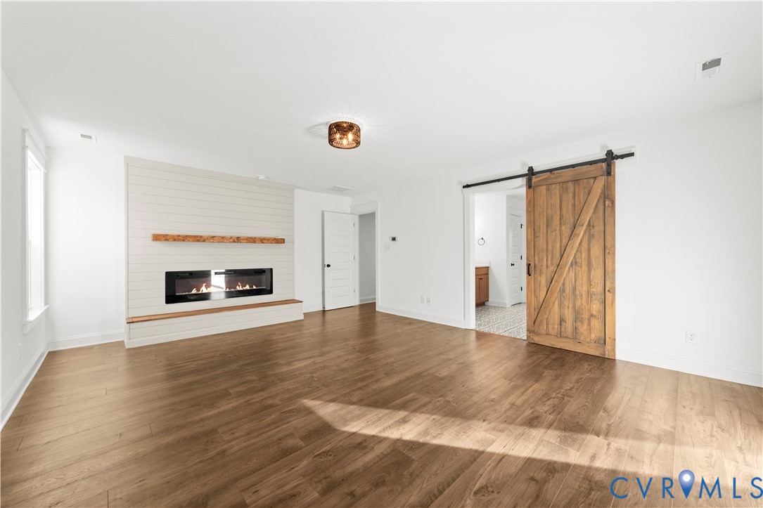 Wood-finish flooring, horizontal shiplap fireplace surround, built-in wooden mantel, inset linear electric fireplace, and sliding wooden barn door