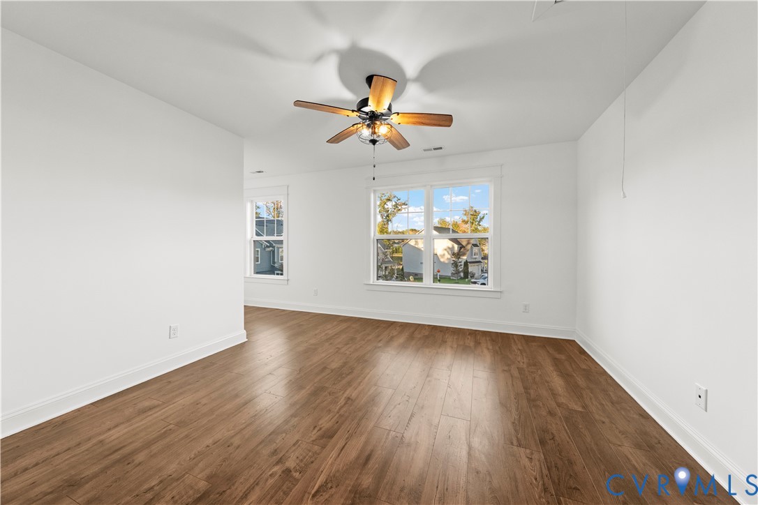 Room featuring wood-finish flooring, white walls, dual-pane windows, and a ceiling fan with integrated lighting