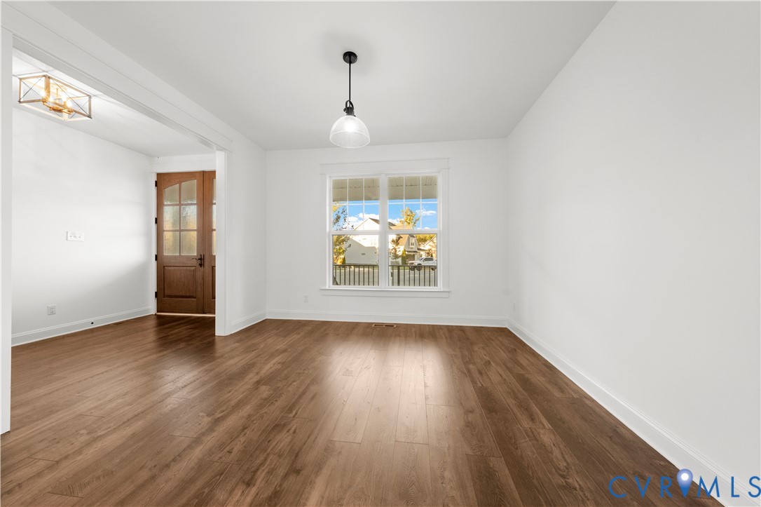 Wood-finish flooring, central pendant lighting, recessed entry door with glass paneling, and multi-pane window