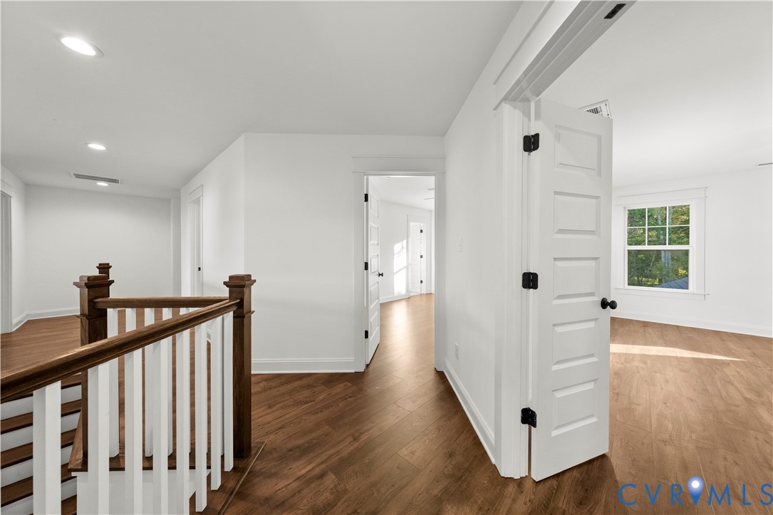 Interior landing featuring wood-finish flooring, recessed lighting, white five-panel doors, and a wood-capped staircase with white balusters