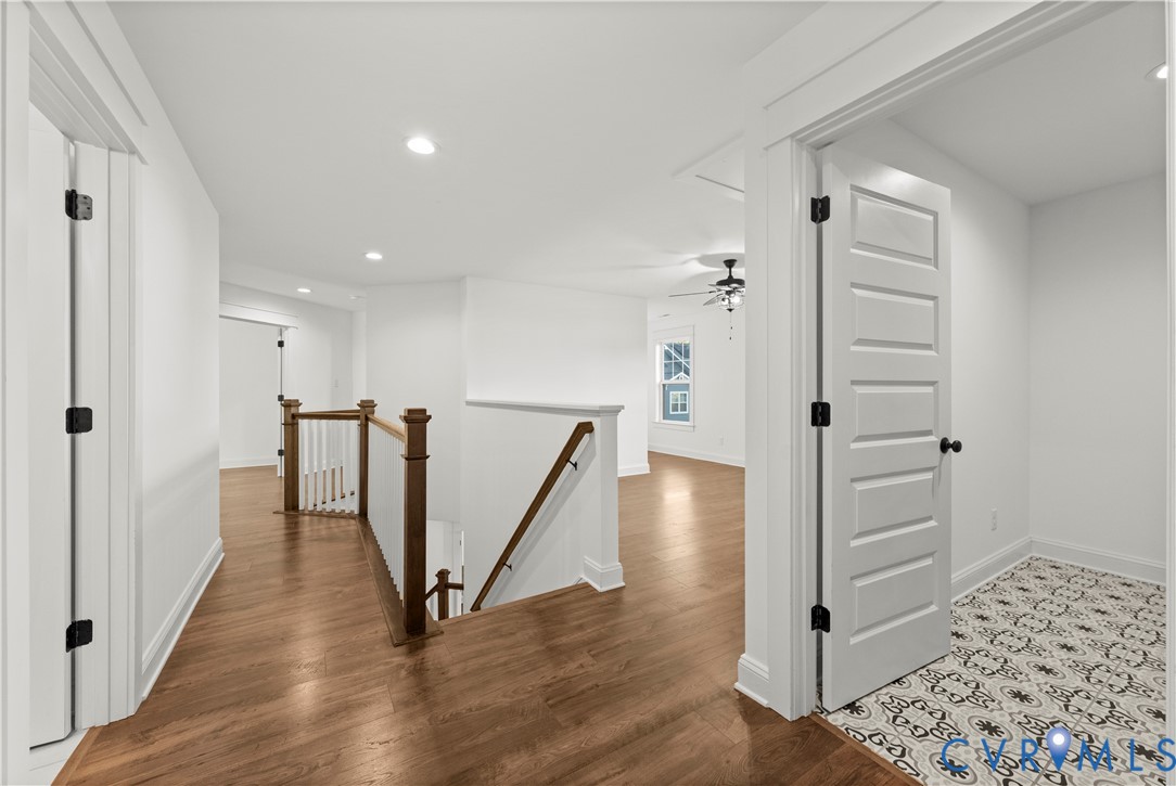 Wood-finish flooring, staircase with a wood handrail and white balusters, five-panel interior doors, and patterned tile flooring