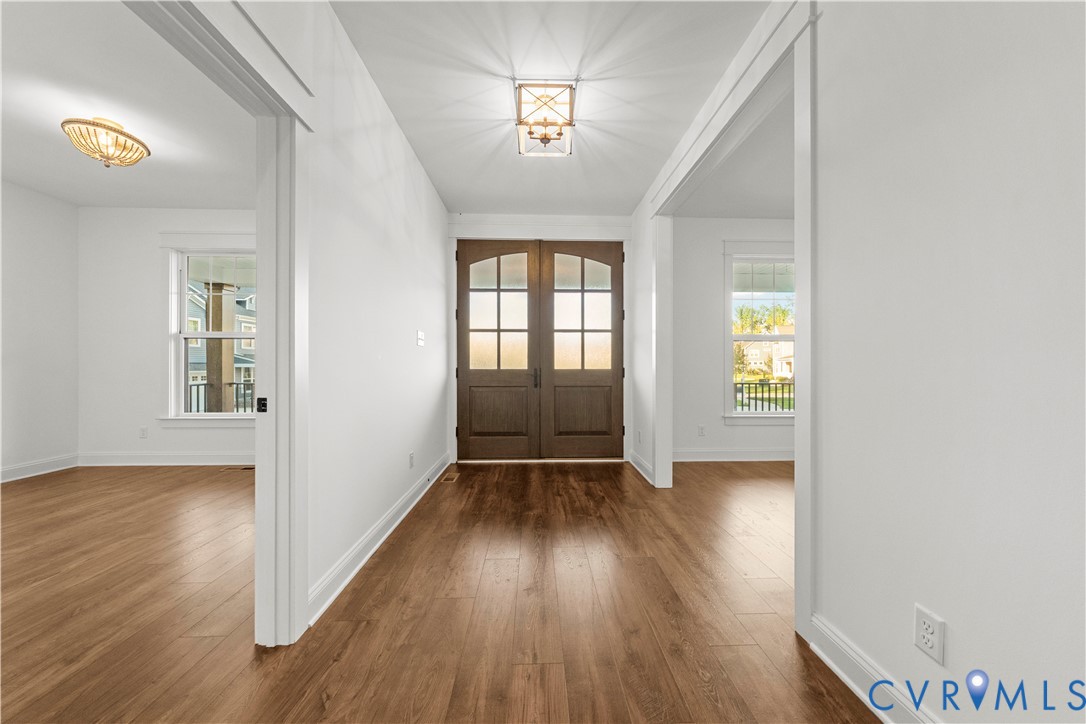 Double entry doors featuring glass paneling, wood-finish flooring, and multi-light geometric ceiling fixtures
